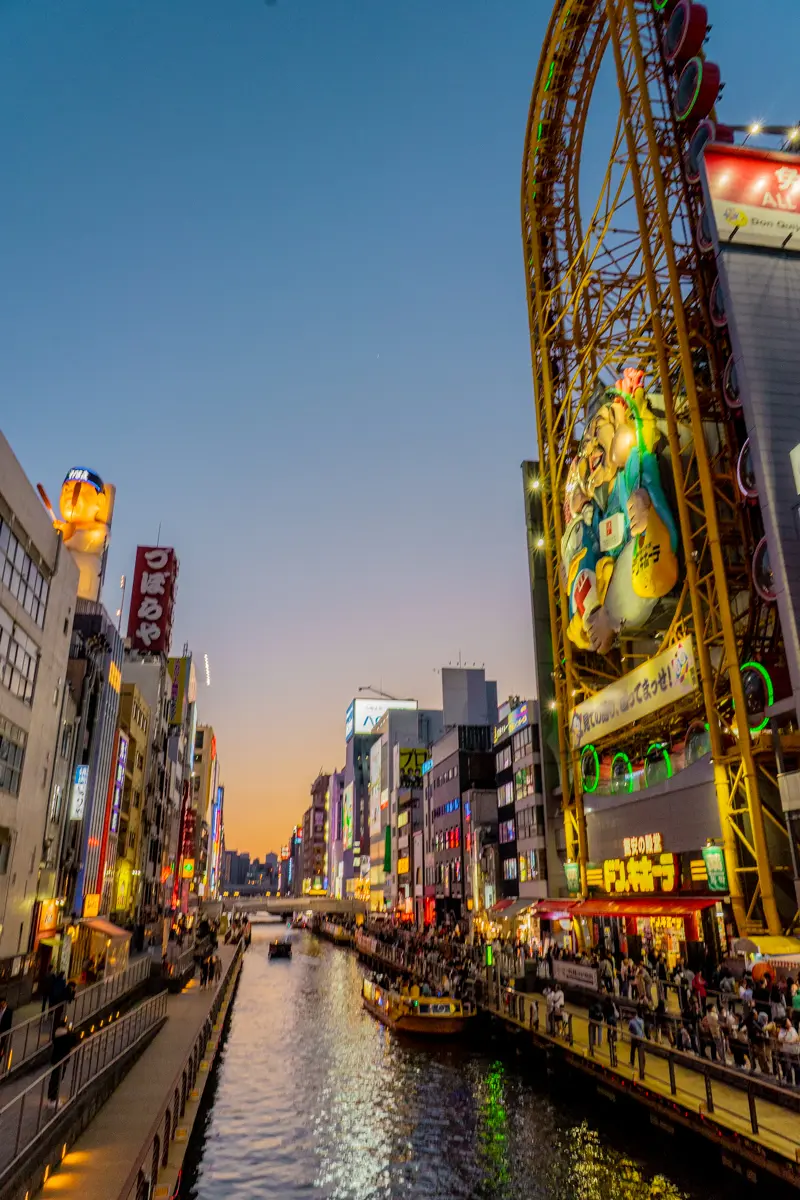 Dotonbori canal at night in Osaka, Japan with neon-lit signs, food stalls, and crowds.