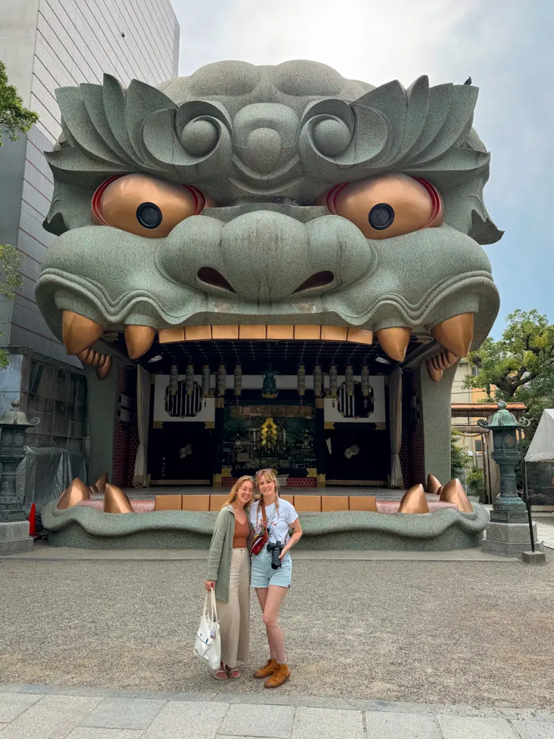 A large lion-headed temple entrance at Namba Yasaka Shrine in Osaka, with two women posing in front.