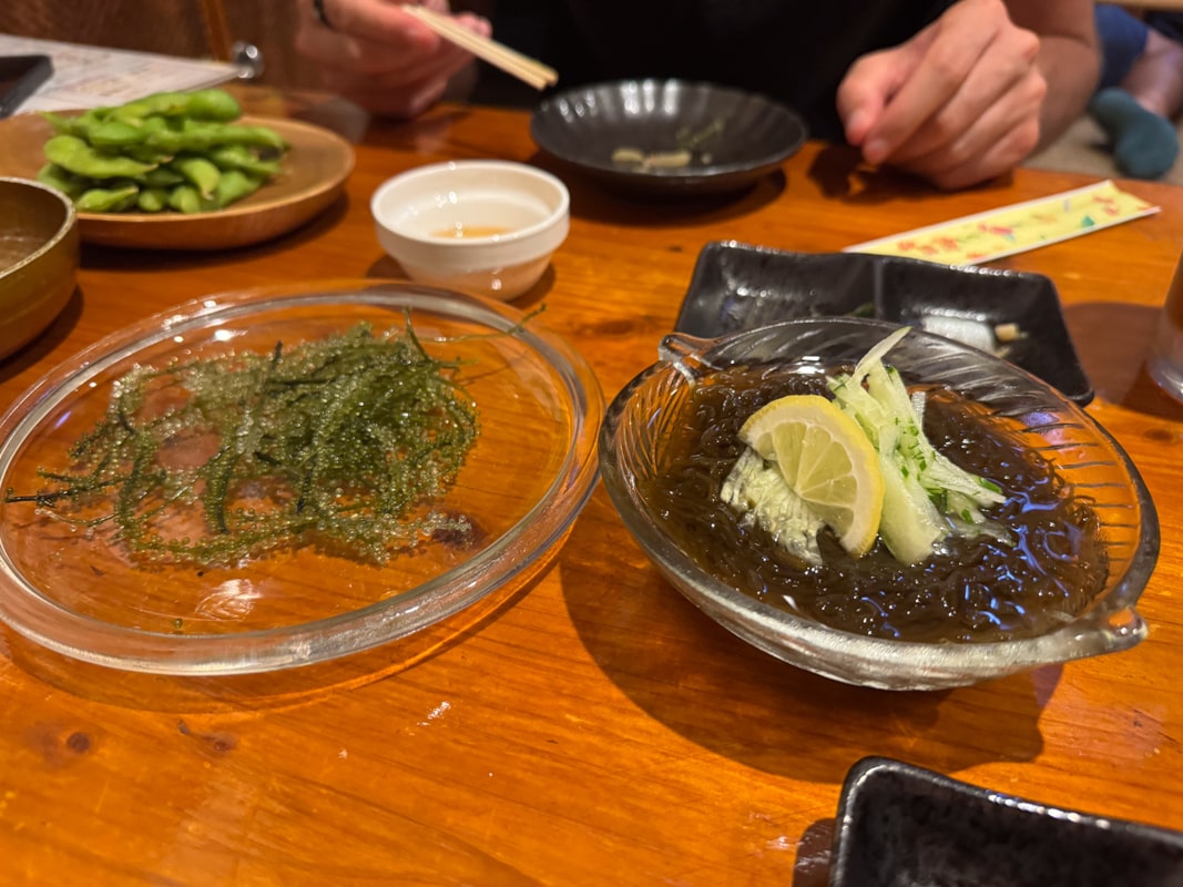 A wooden table in a Miyakojima restaurant with plates of sea grapes (umibudo) and seaweed (mozoku).